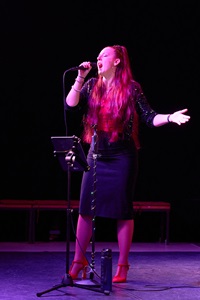 Linda Jesse singt stehend in rotem Scheinwerferlicht vor dunklem Hintergrund